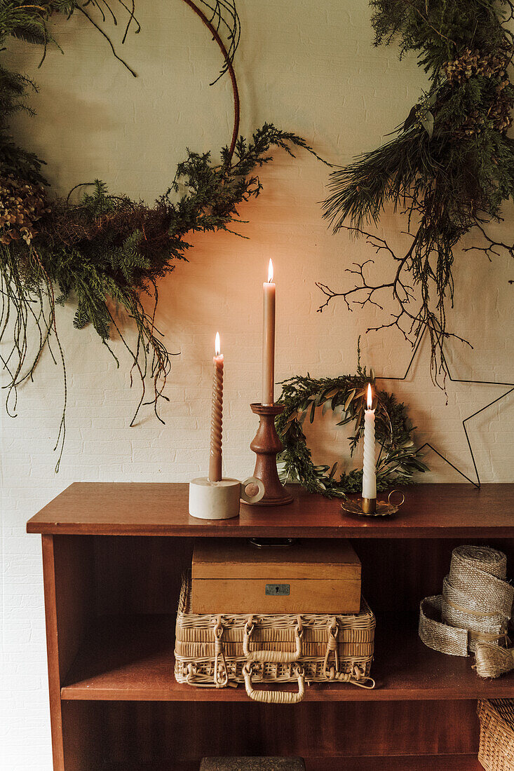 Wooden shelf with lit candles and Christmas wreaths in the background