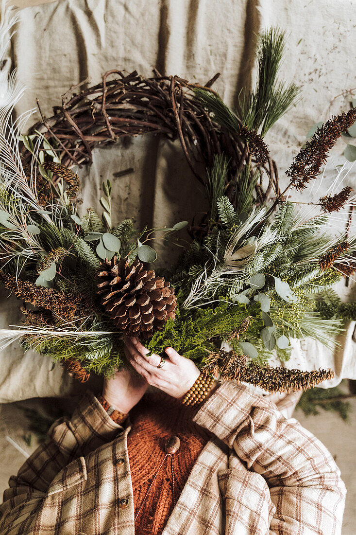 Person holds natural wreath made from twigs and cones