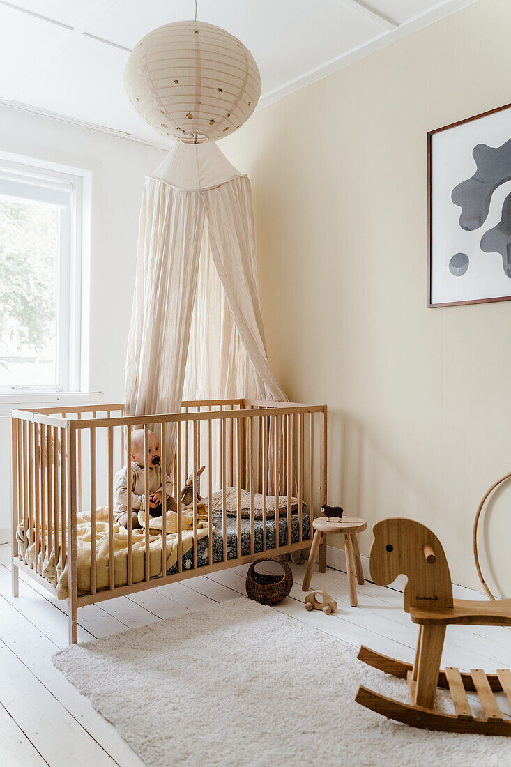 Baby room with light-colored wooden cot, canopy and rocking horse