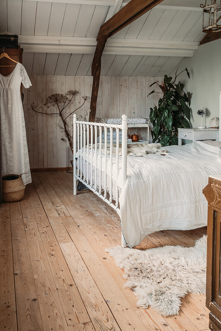 Bedroom with wooden floorboards, white bed and sloping ceiling