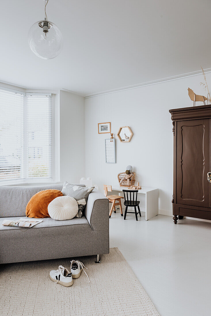 Light-flooded living room with grey sofa and vintage cupboard