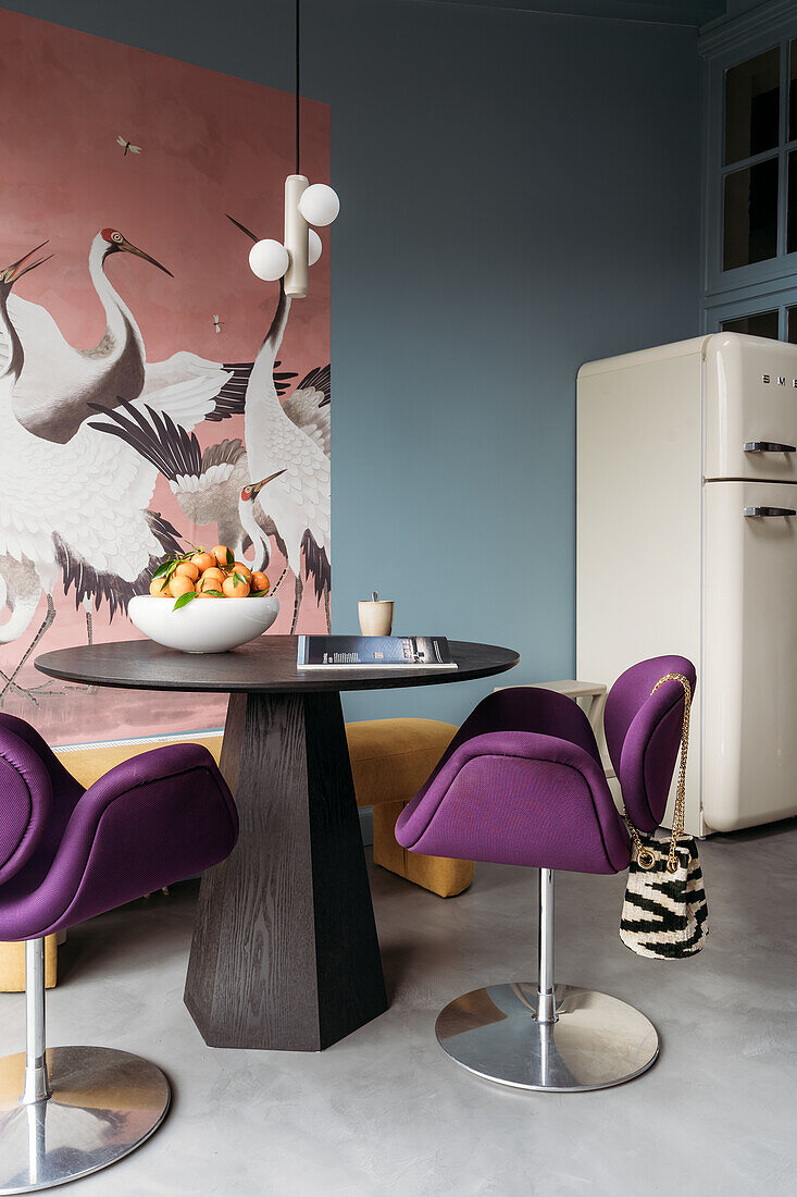 Round dining table with purple swivel chairs in front of wallpaper with herons