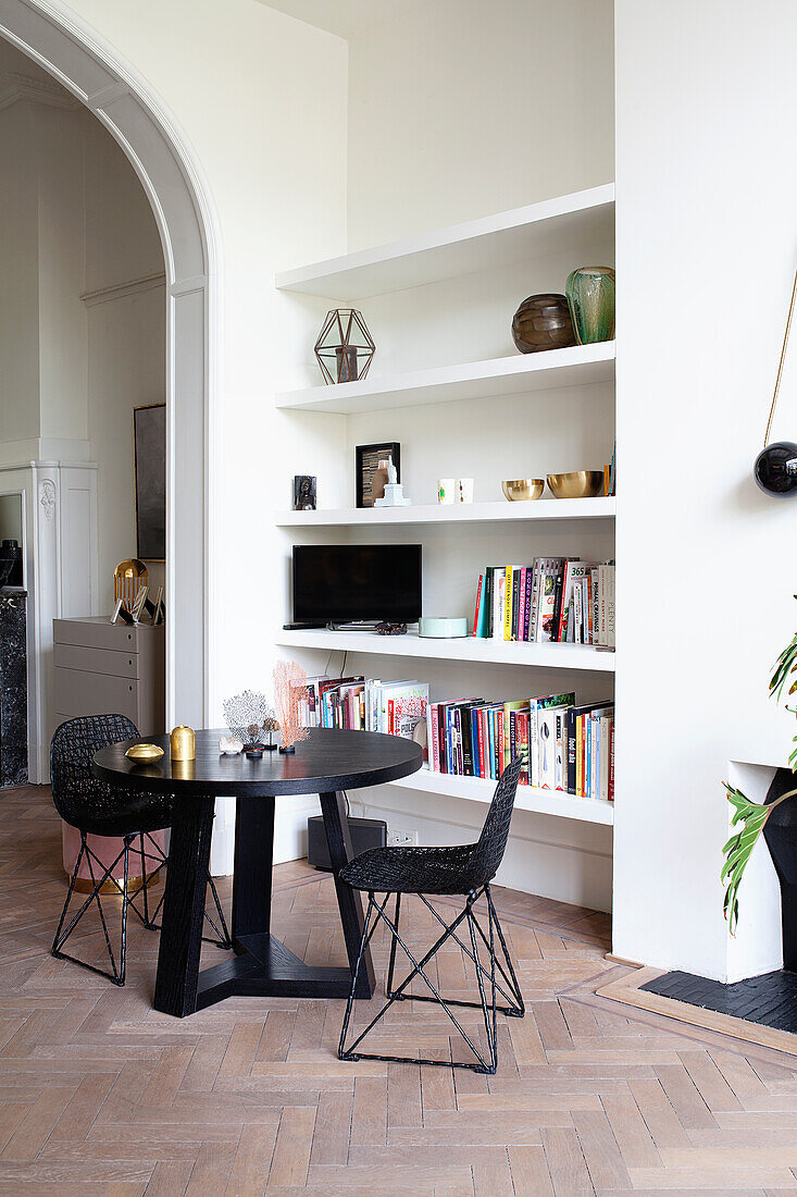 Round table with black chairs in front of white built-in shelves