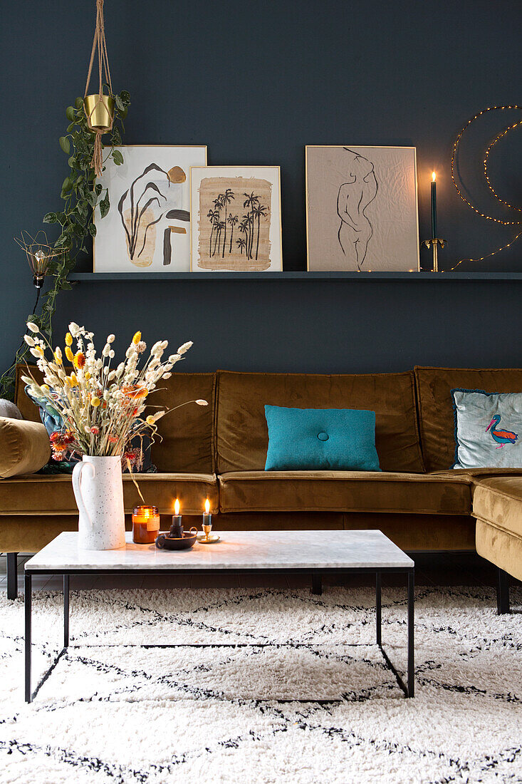 Velvet sofa and shelf with pictures on dark blue wall in living room