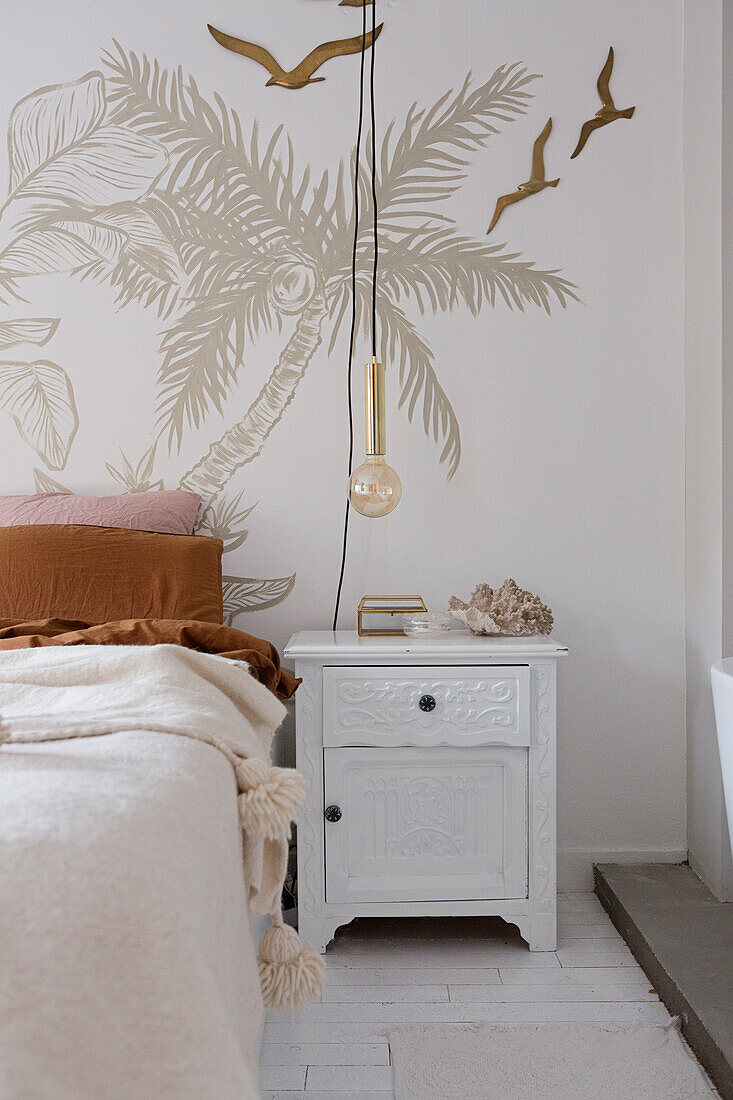 Bedroom with palm tree wall decoration and white bedside table