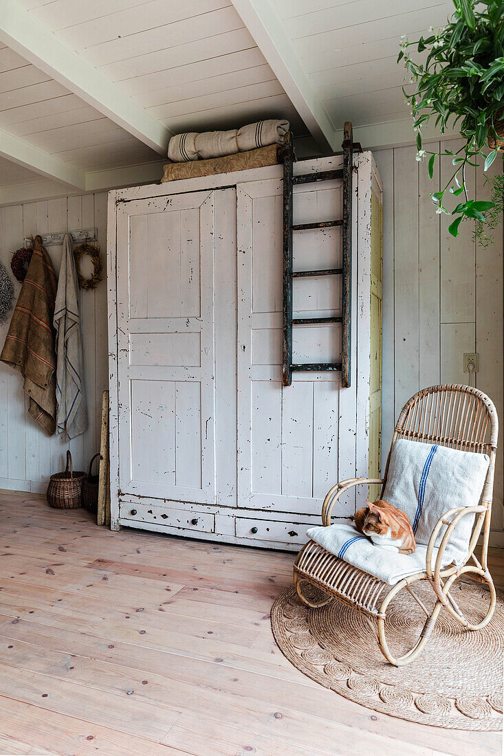 Shabby chic cupboard, rattan armchair on round carpet and wooden floorboards