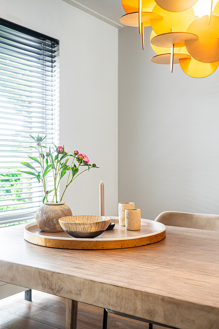 Wooden table with round tray, candles and vase in modern dining room