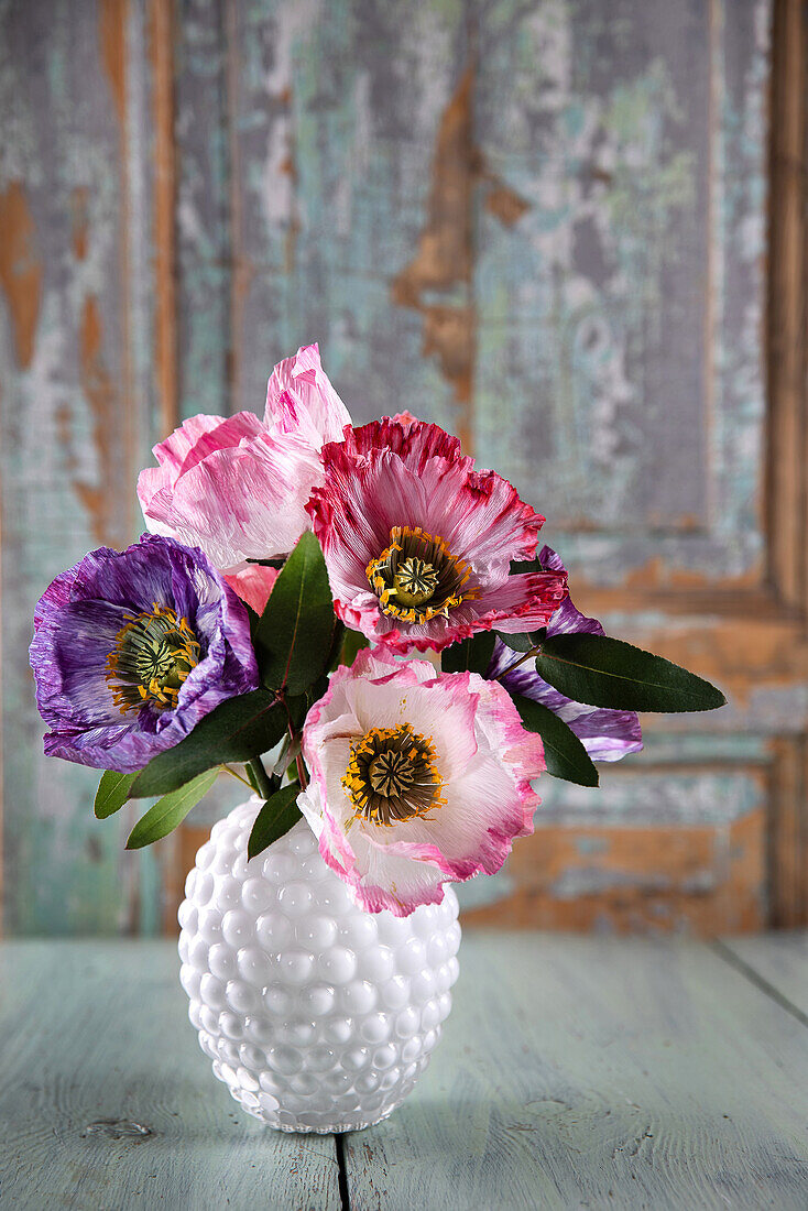 Paper poppies in white ceramic vase in front of wooden wall