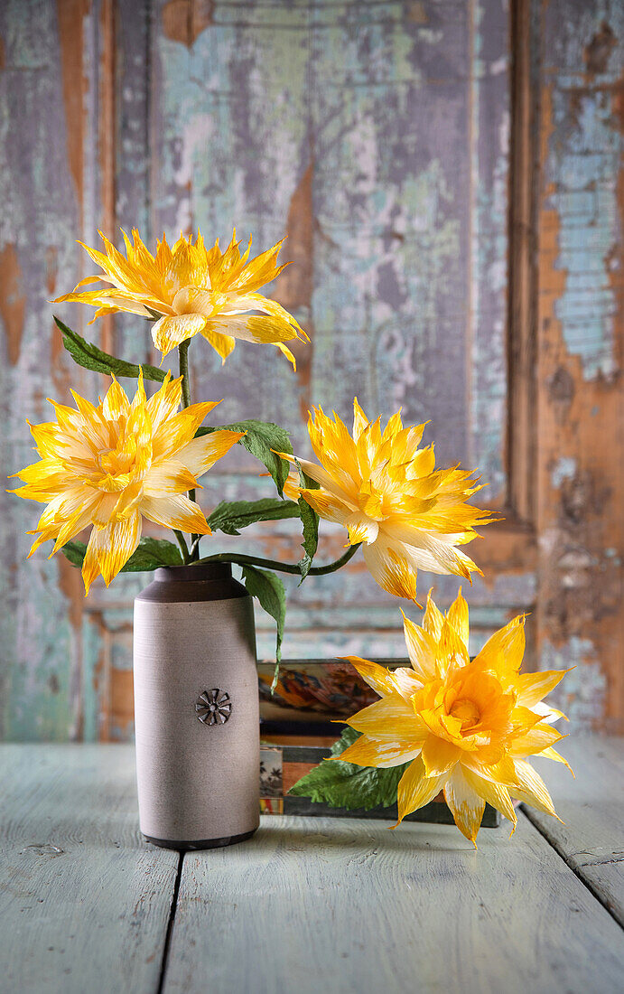 Yellow dahlias in a vase in front of a rustic wooden wall