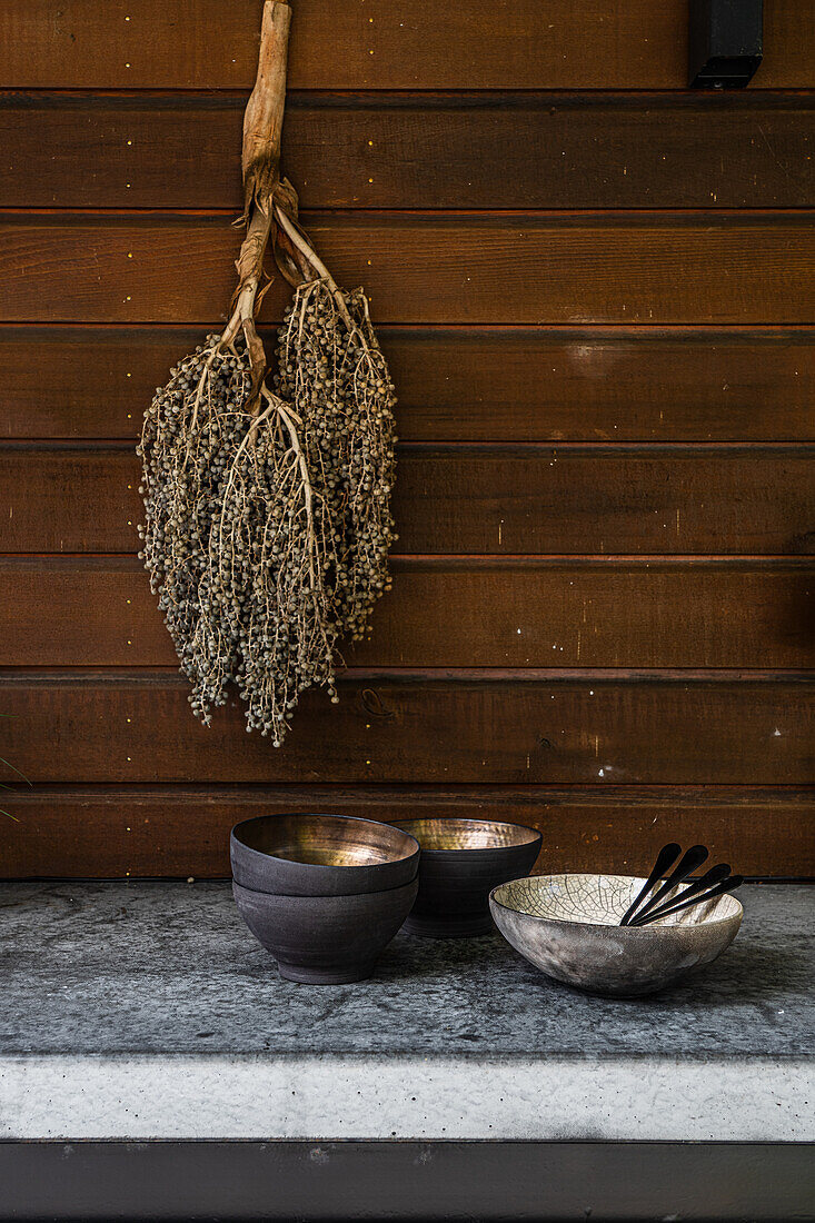 Wooden wall with hanging dried flowers and bowls on a stone table