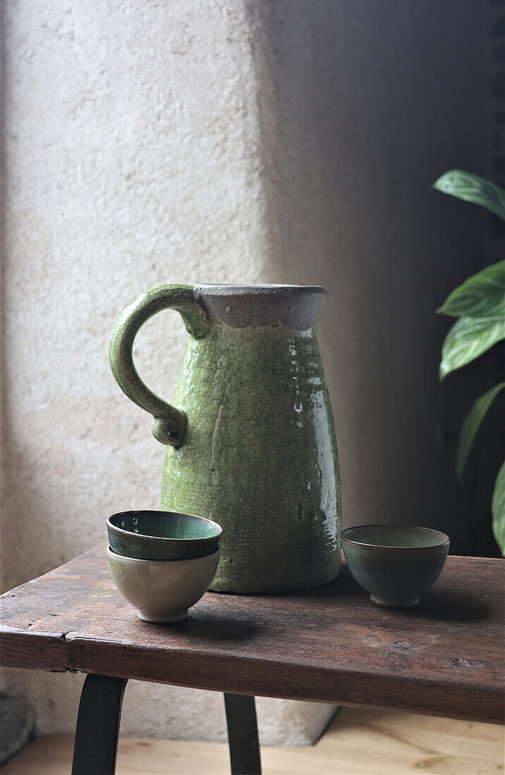 Green ceramic jug and bowls on wooden bench