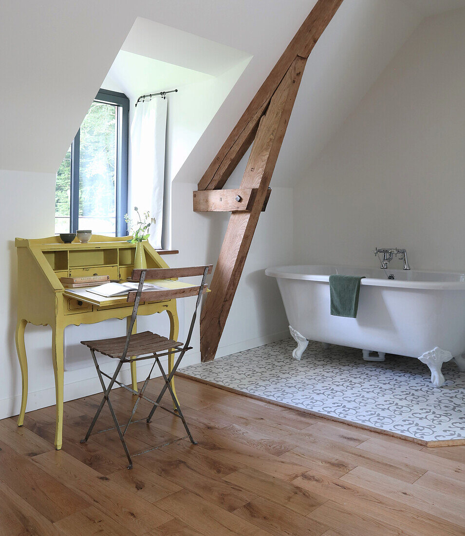 Free-standing bathtub with lion's feet next to yellow secretary in the attic