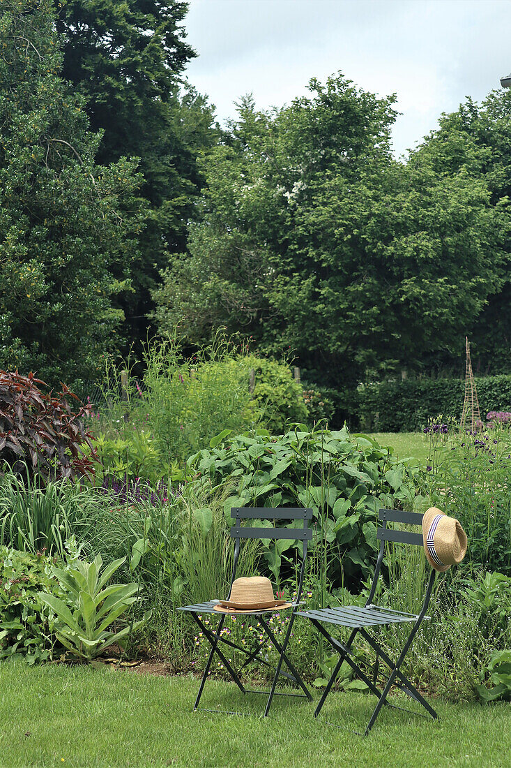 Garden with two metal chairs and summer hats in front of lush plants