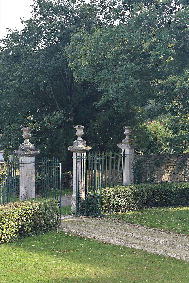 Iron gate with stone pillars in a well-tended garden