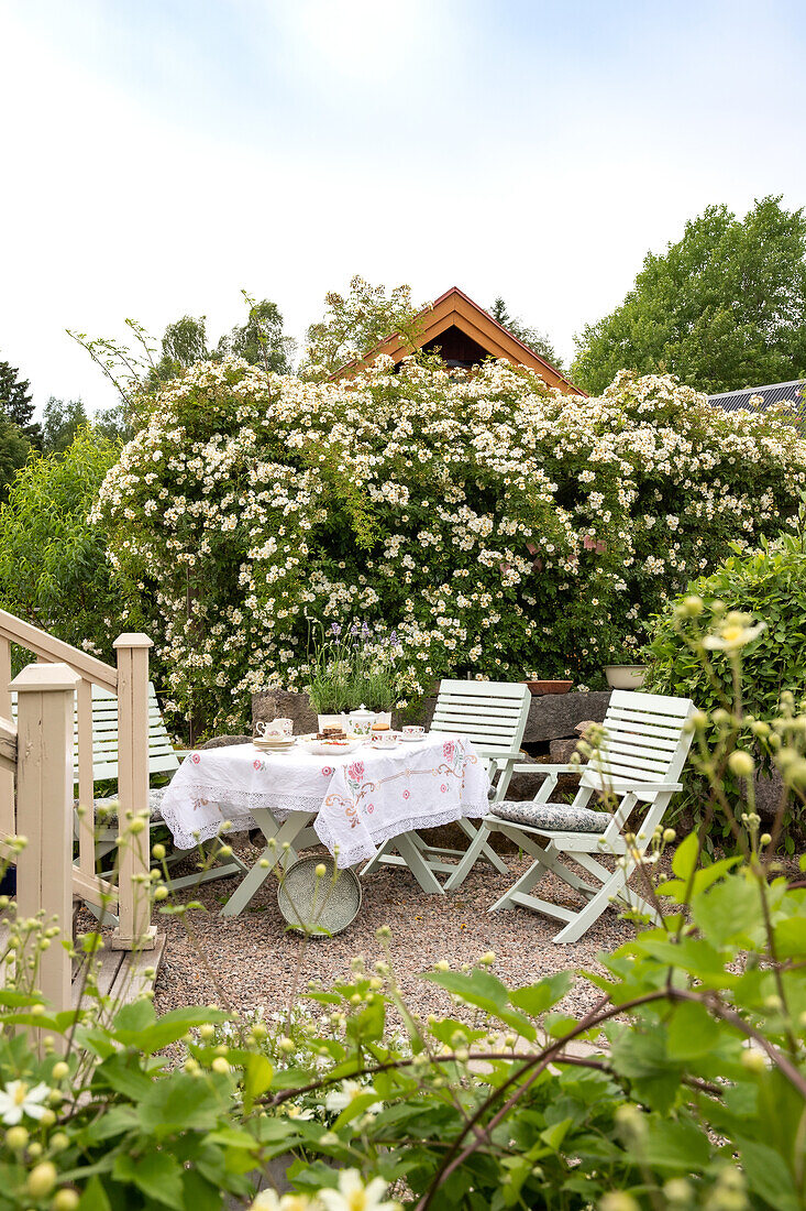 Terrasse mit blühendem Strauch, gedeckter Gartentisch