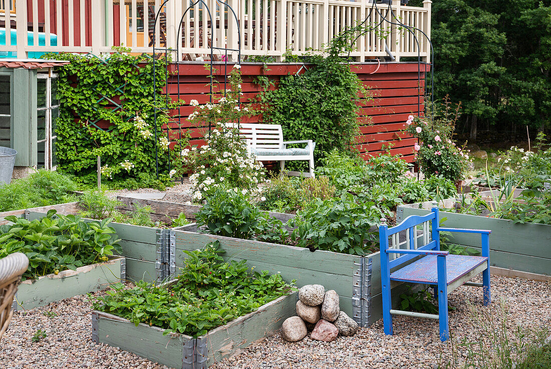 Gartenbänke und Hochbeete vor rotem Haus mit Veranda