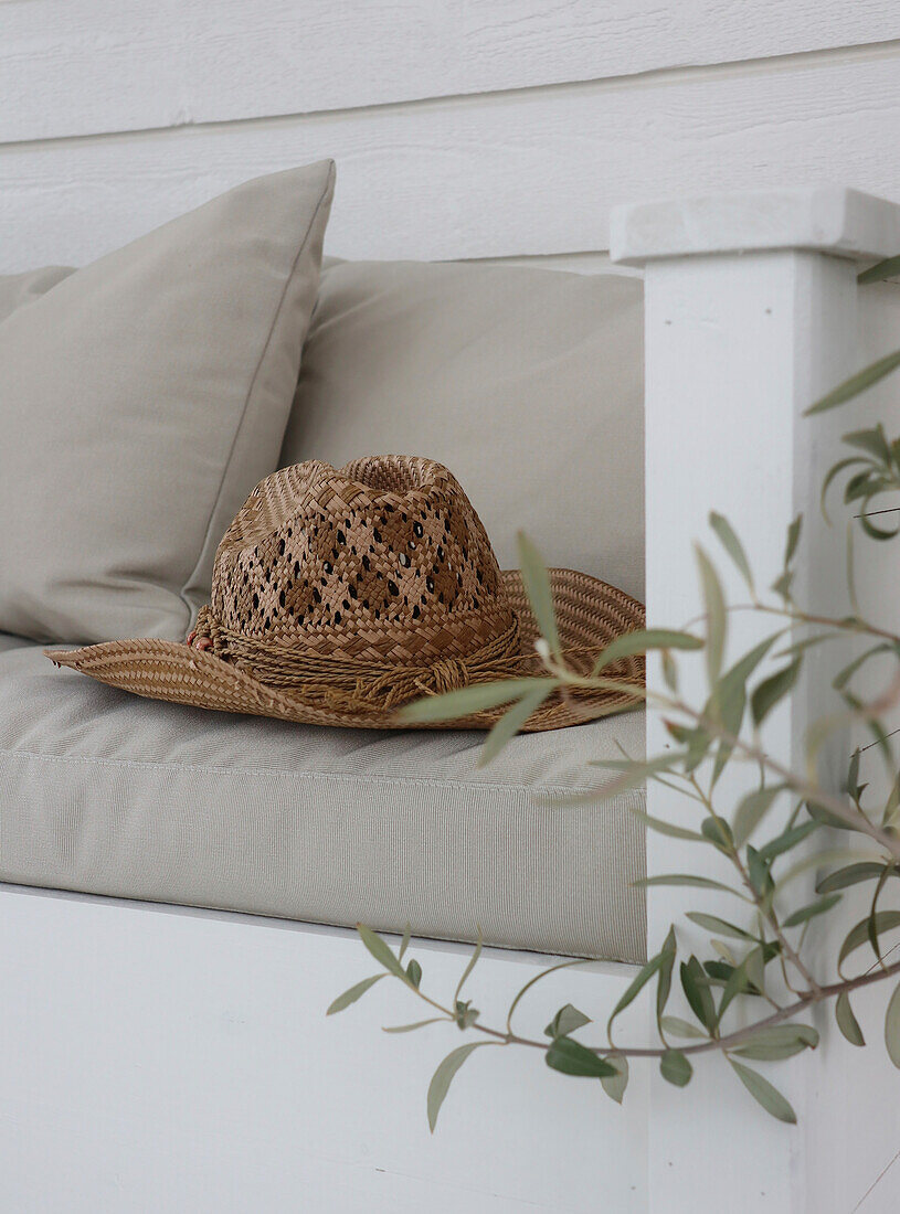 Straw hat on white bench with cushion, olive branches