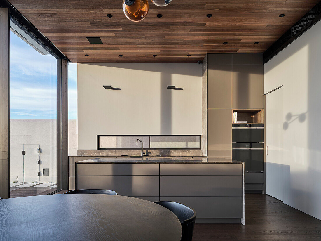 Modern kitchen with kitchen island and round dining table, wooden ceiling and large window front