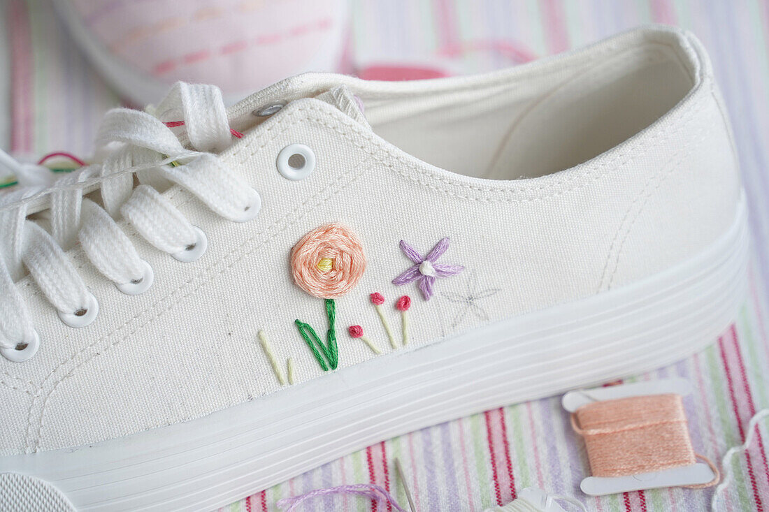 White canvas shoes with hand-embroidered floral motifs on a striped base