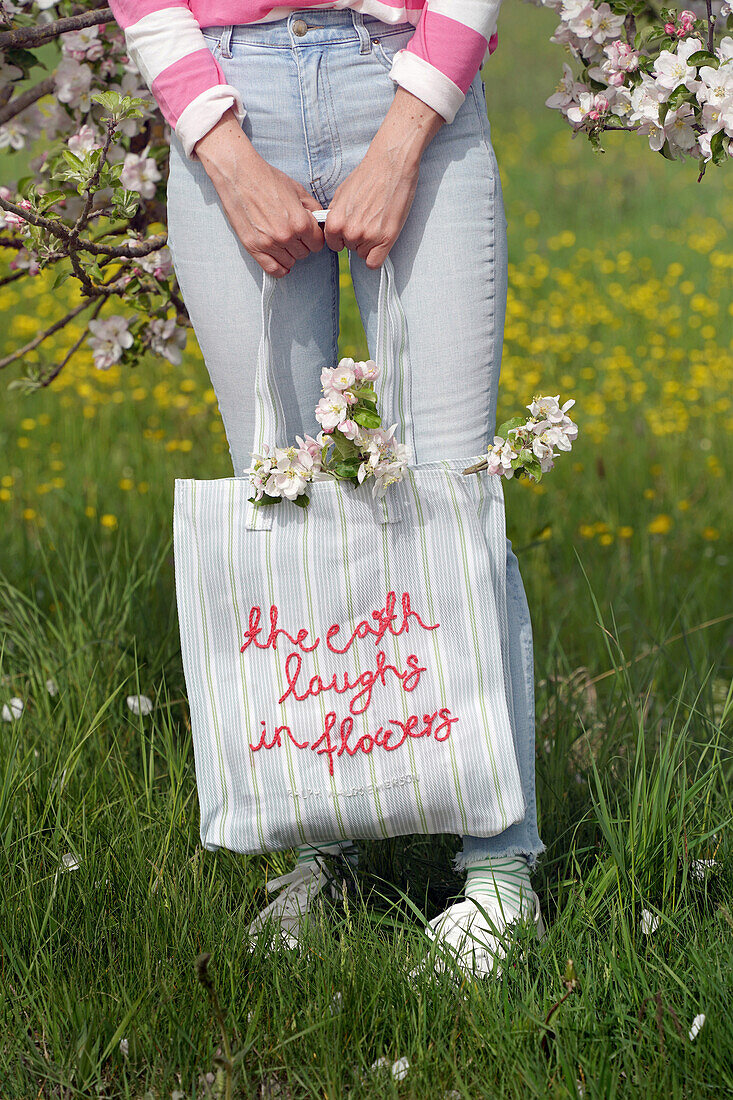 Striped fabric bag with embroidered lettering and blossoming branches in spring