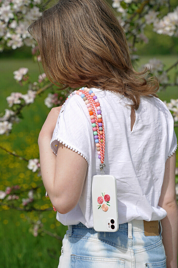 Woman with smartphone and mobile phone necklace with colourful beads in the garden in spring