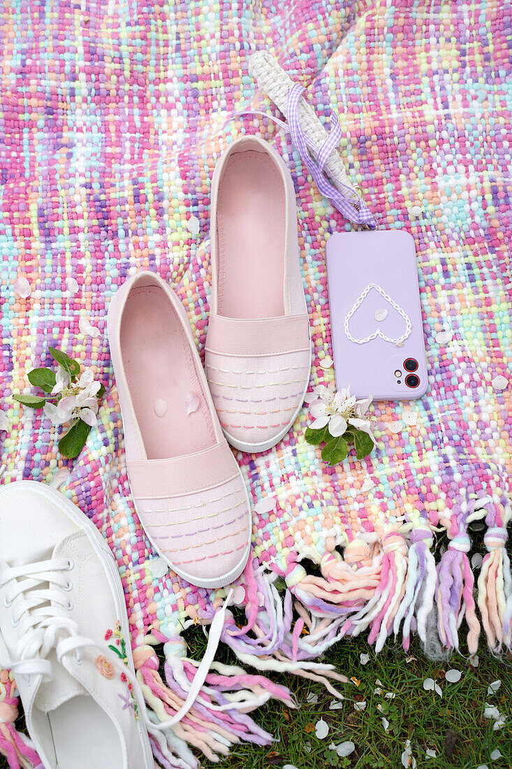 Pink and white shoes next to smartphone on colourful picnic blanket