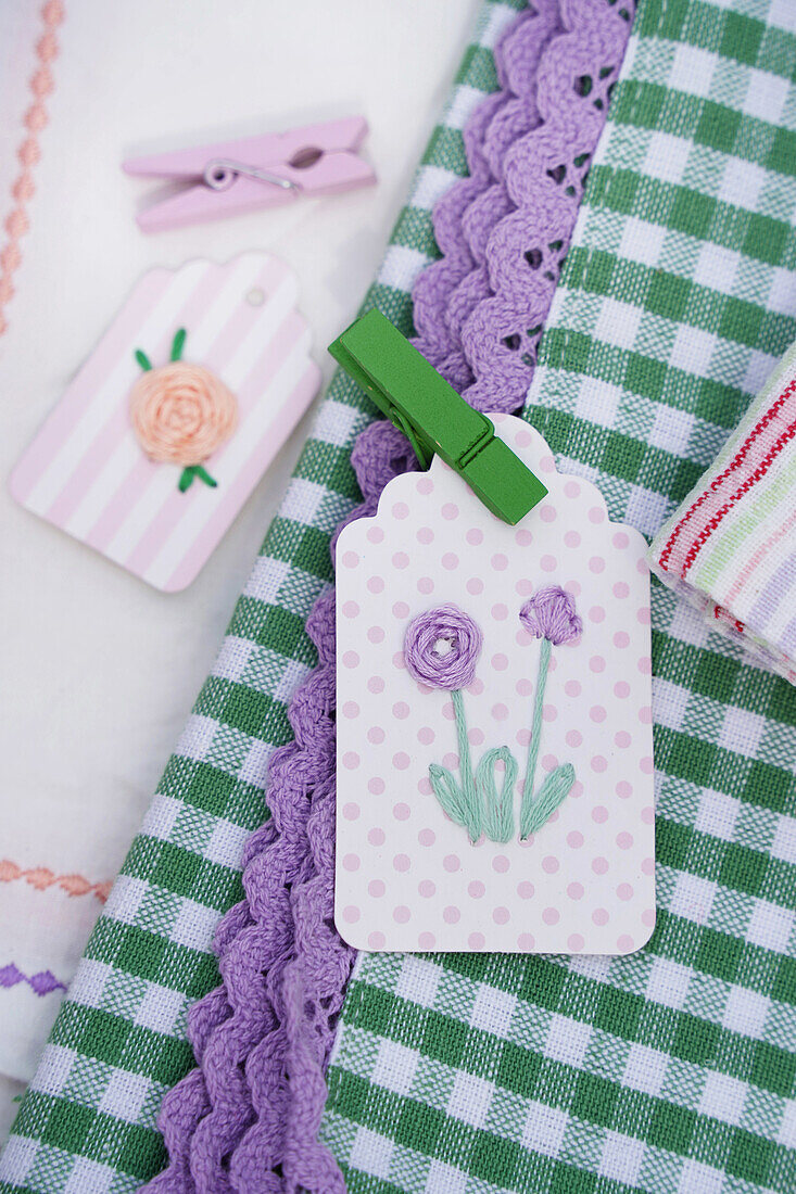 Embroidered pendant with flower motif and green wooden clip on chequered tablecloth