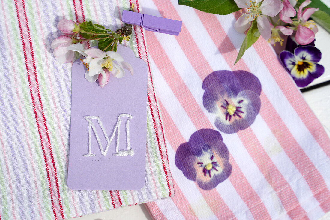 Striped towel with pansy motif and lavender-coloured pendant with letter ""M