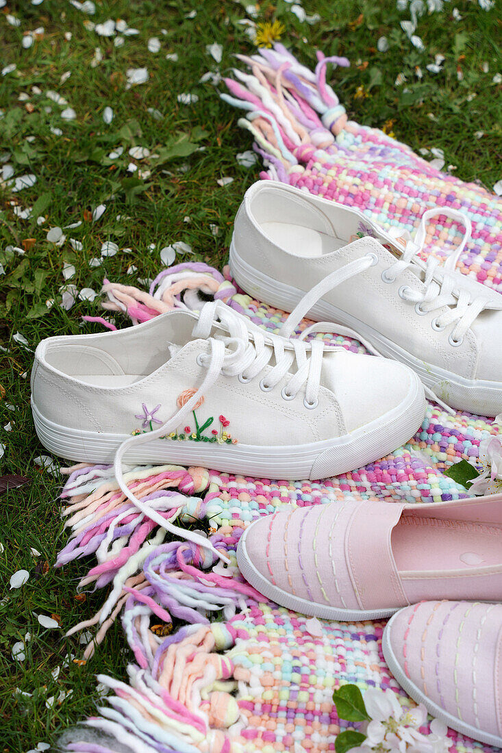 Embroidered white sneakers and pink slippers with embroidery on a colourful blanket in the garden