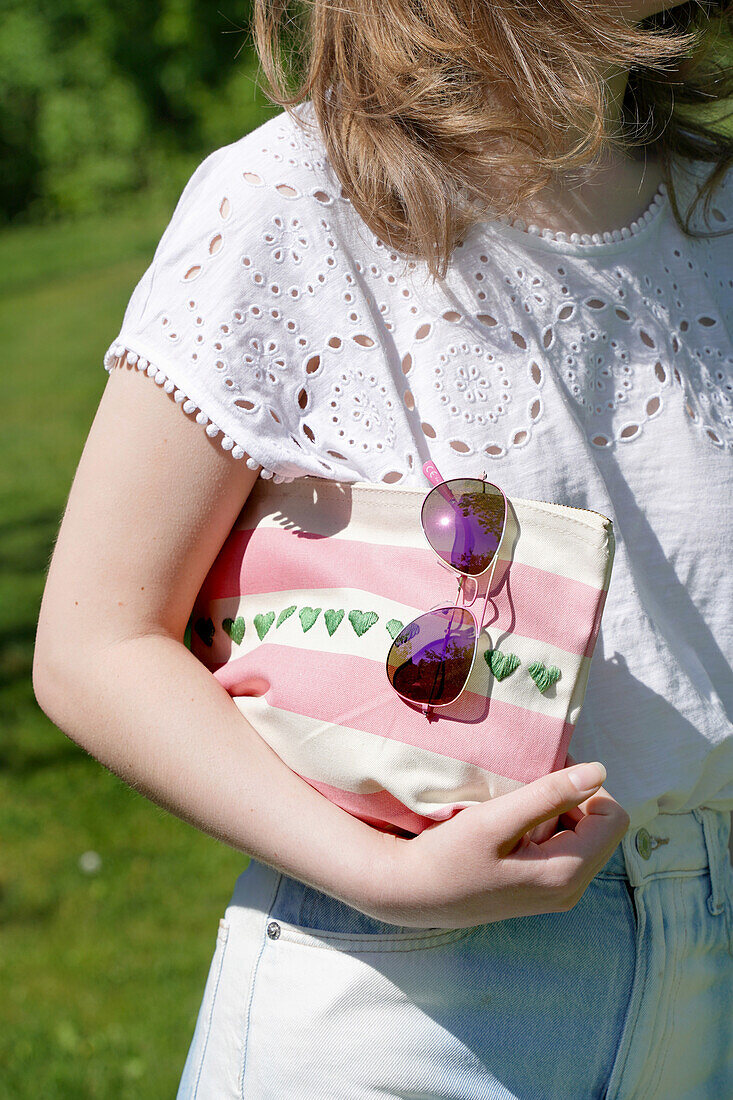 Person with white lace blouse and striped bag with embroidered hearts outdoors