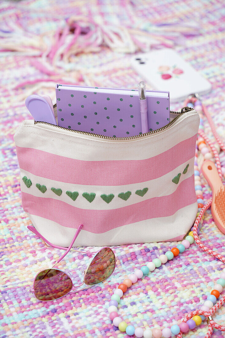 Striped bag with embroidered hearts, notebook and sunglasses on a colourful blanket