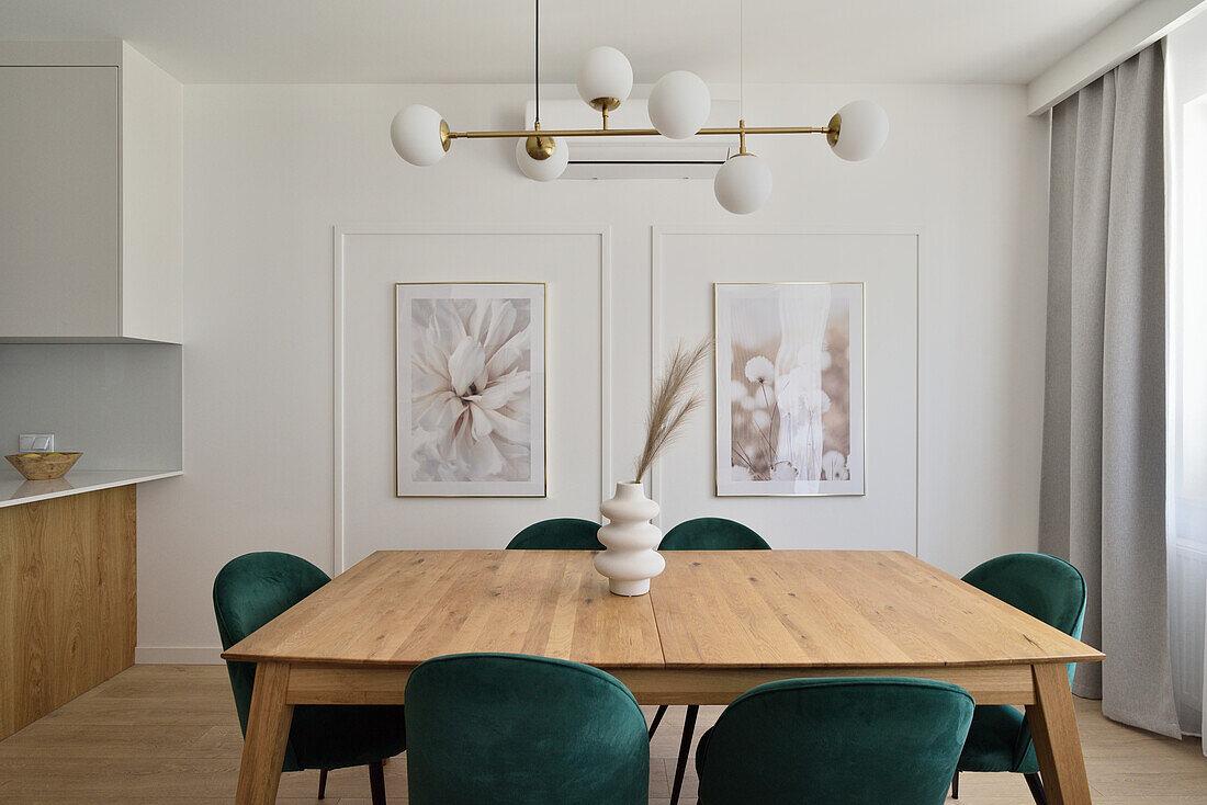 Dining room with light-colored wooden table, green velvet chairs and modern pendant light