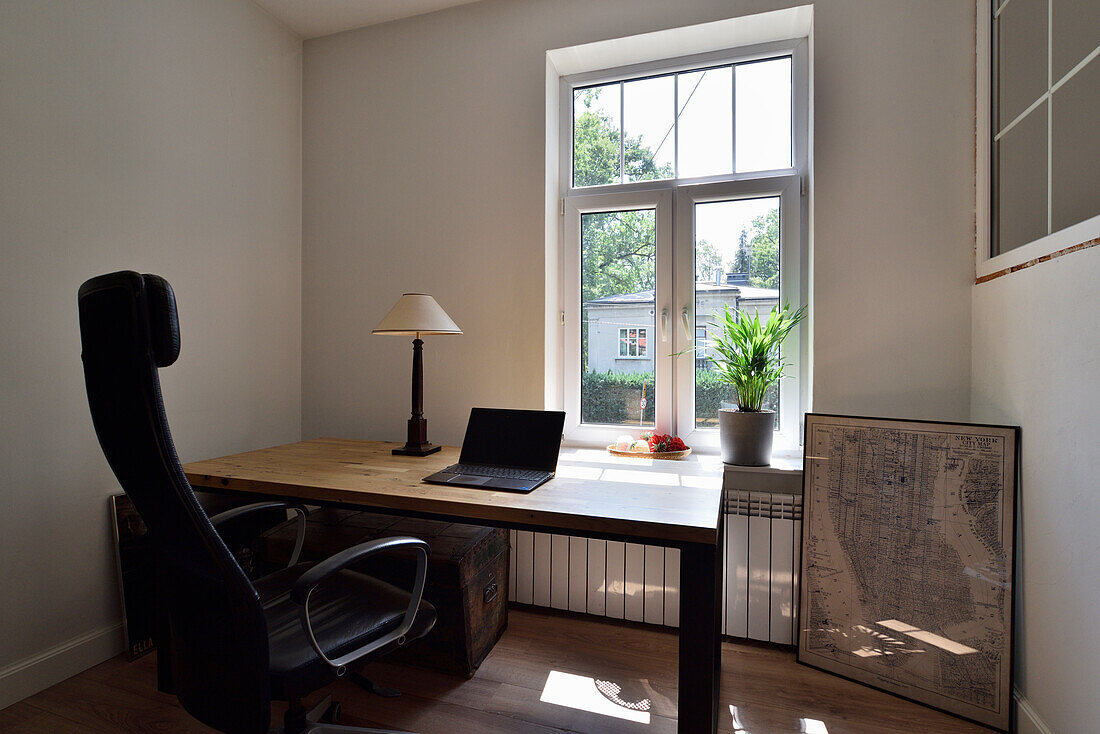 Home office with wooden table, desk chair and laptop in front of a large window