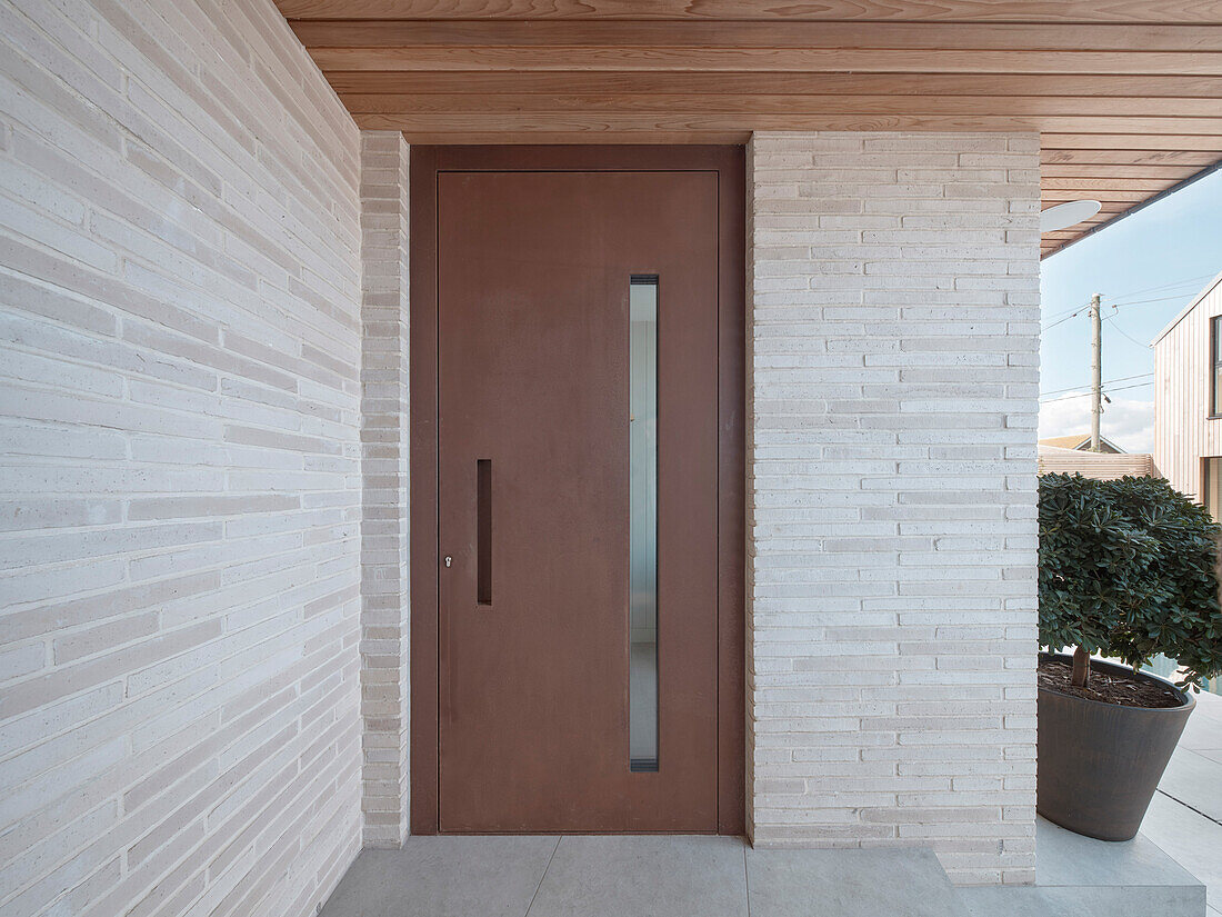 Front door with glass insert and light-colored brick paneling at house entrance