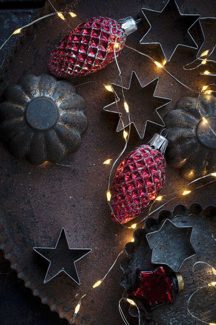 Old biscuit tins on a baking tray with red Christmas tree decorations and fairy lights