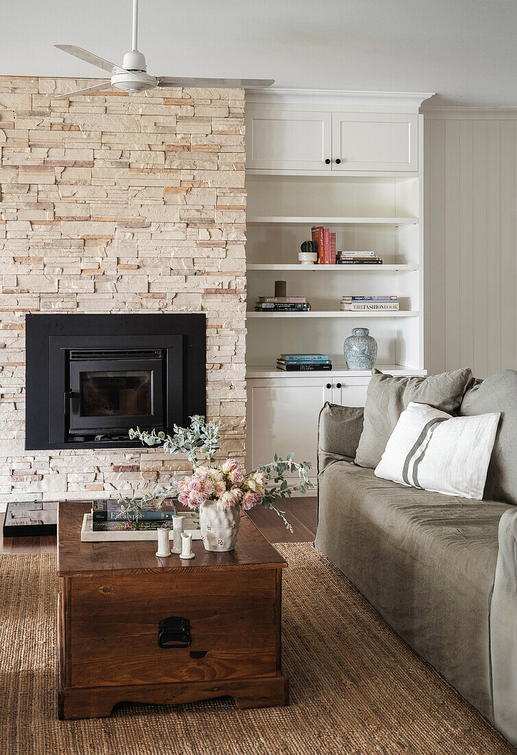 Living room with fireplace, stone chimney, light grey sofa and chest as coffee table