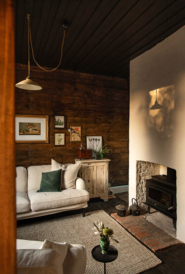 Rustic living room with white sofa, dark wooden walls and corner fireplace