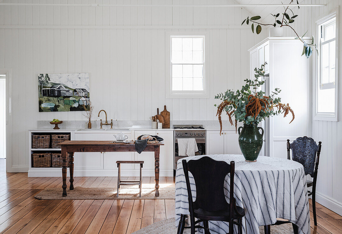 Country kitchen with white wood paneling and rustic dining table with striped tablecloth