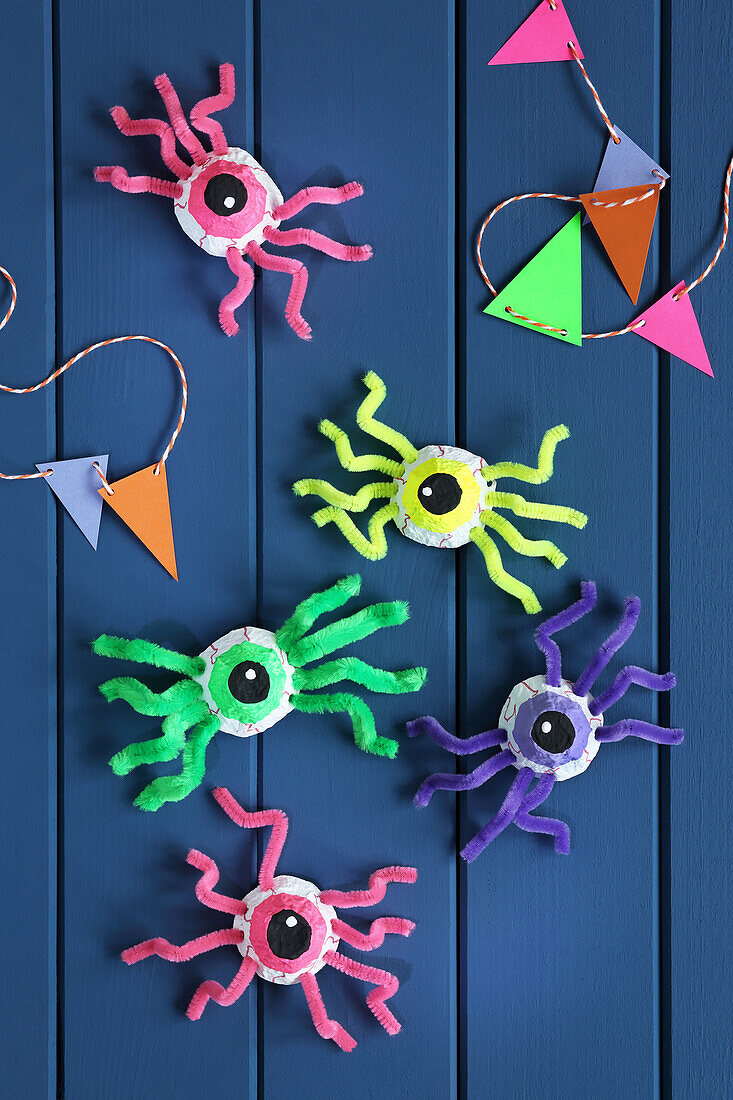 DIY spy spiders made from egg carton and pipe cleaners on a blue wooden wall