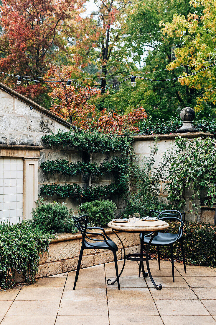 Terrace with round table and metal chairs, surrounded by green plants