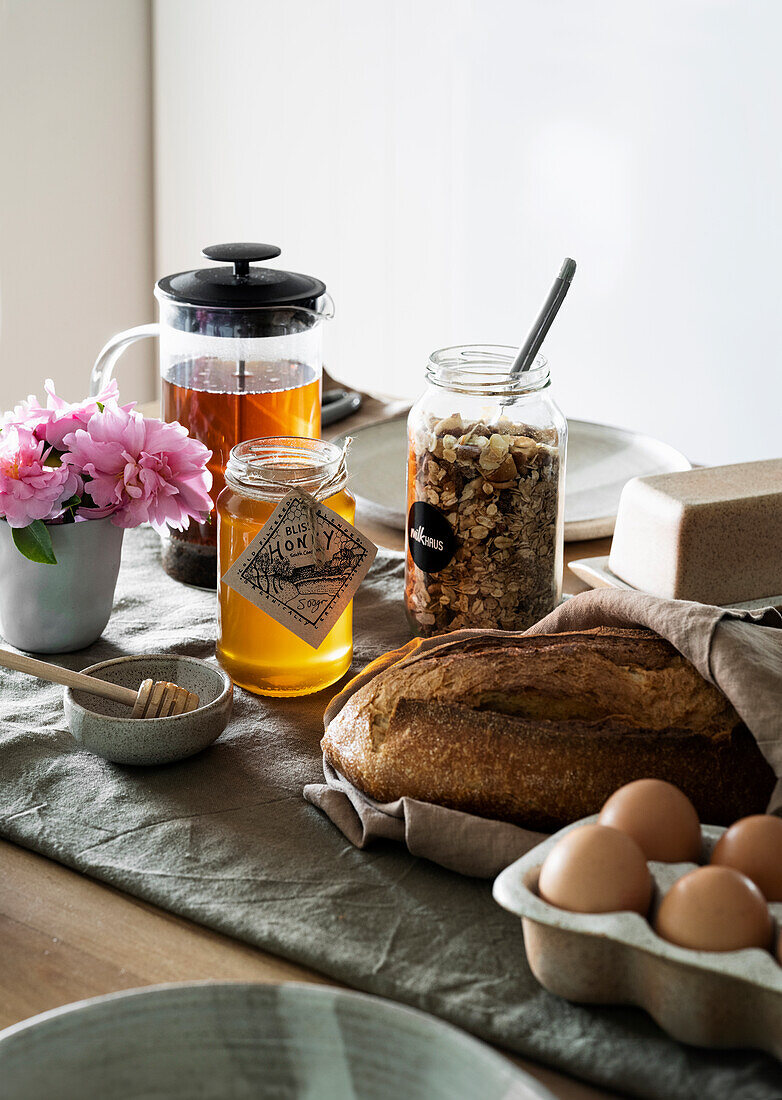 Breakfast table with fresh bread, eggs, honey, muesli mix and tea