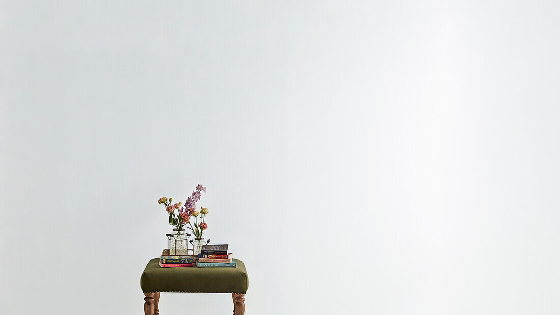 Small stool with flowers and books in front of white wall