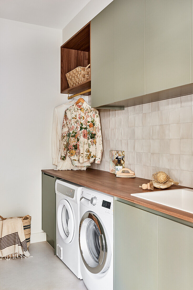 Modern laundry room with pastel green cabinets and wooden accents