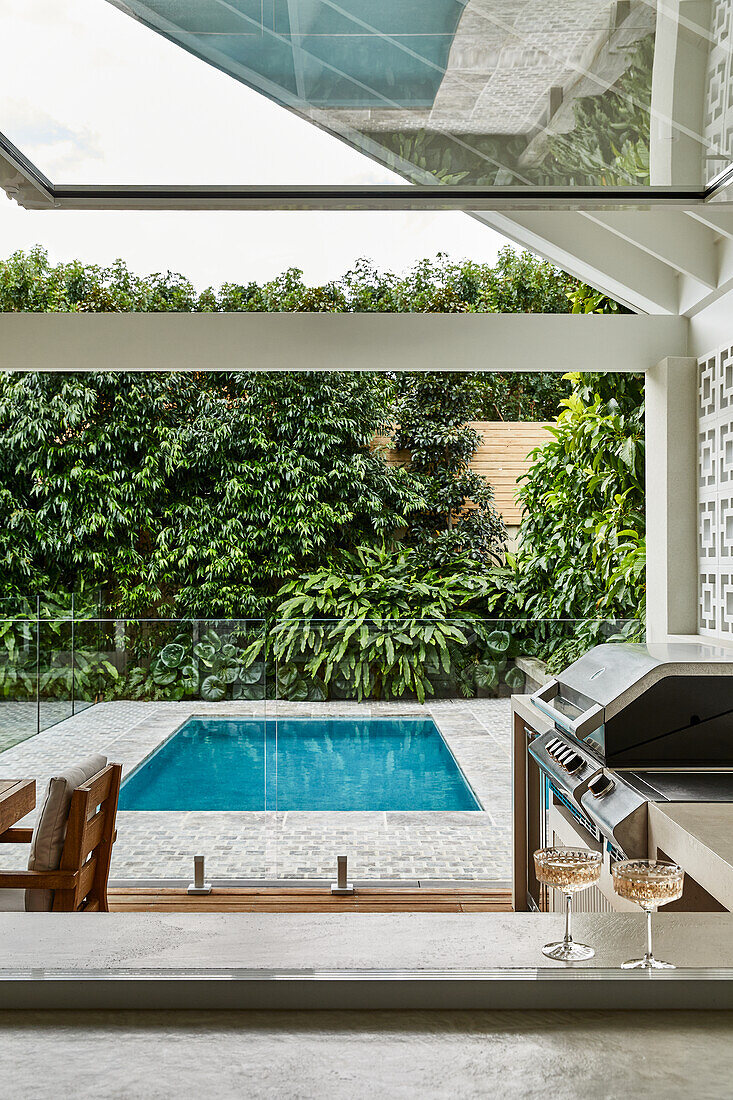 View of modern pool area with glass railing and outdoor kitchen