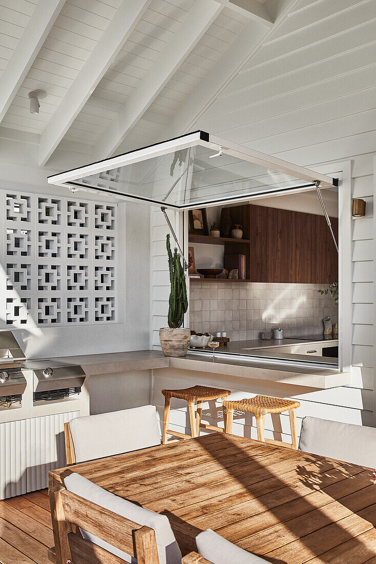 Dining area on terrace with wooden table, folding window to modern outdoor kitchen