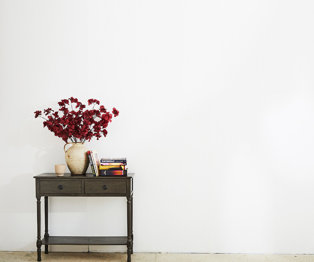 Dark side table with red flower arrangement and books