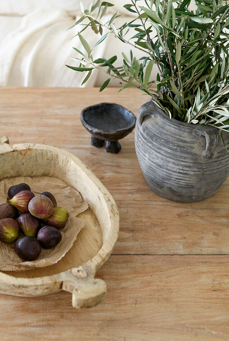 Holztisch mit Feigen und Olivenzweigen in Keramikvase