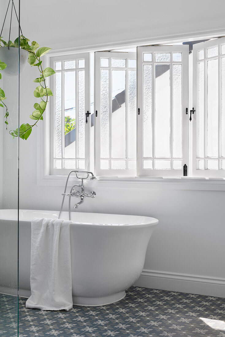 Freestanding bathtub in front of mullioned windows in the bright bathroom