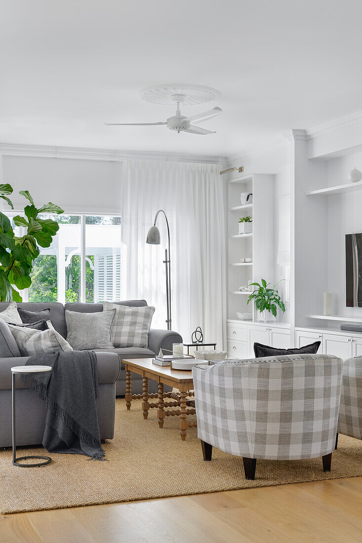 Grey sofa and chequered armchairs in the bright living room with ceiling fan