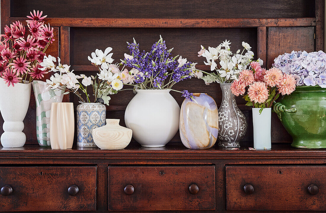 Various flower arrangements in vases on an antique wooden shelf